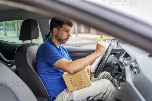 Side view from inside a vehicle of a serious delivery man writing and inventorying packages on a car