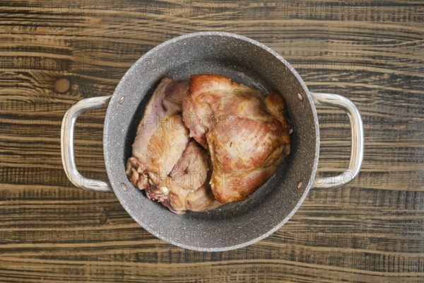 Tender, cooked turkey meat sit in a silver pot on a rustic wooden table, showcasing their golden brown exterior. The kitchen atmosphere highlights a cozy, home-cooked meal vibe.