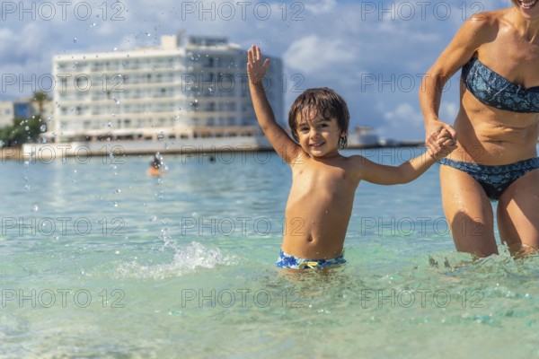 A young boy is splashing in the water with his mother. Scene is joyful and playful