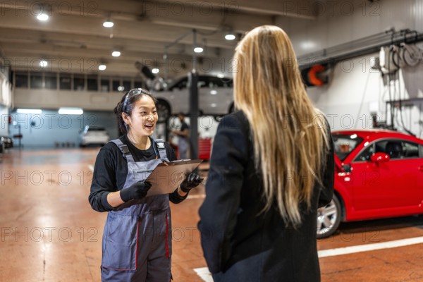 Smiling female mechanic explaining repair details to a customer while delivering a car in a modern auto repair shop