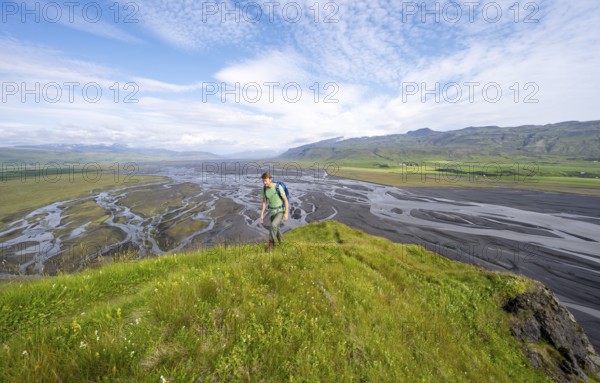 Hiker, young man on a hill, view over alluvial land, meandering river, Dímonarhellir, Suðurland, Iceland, Europe