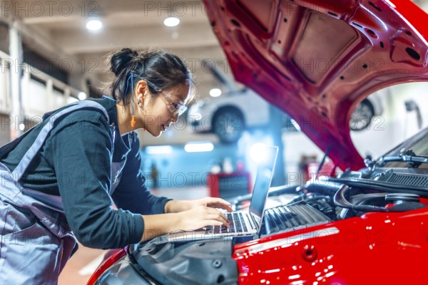 Young female mechanic using a laptop while performing diagnostics on a red car in a modern auto repair shop