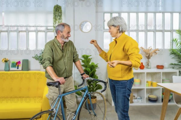 Senior couple talking while holding bike in the apartment. Sustainable way of life