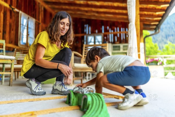 Mom and child enjoying playtime together, building a car track on the porch of their cozy wooden house