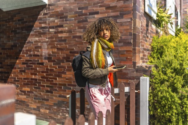 Casual latin woman with curly hair and warm clothes leaving the house using phone