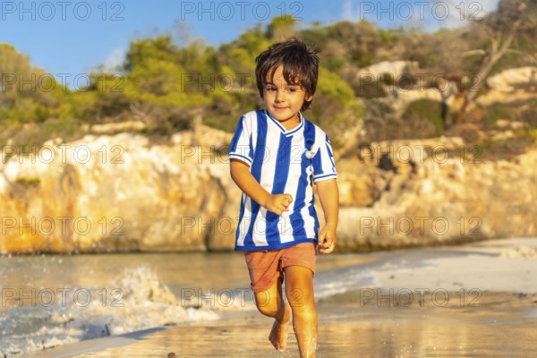 A young boy is running on the beach wearing a striped shirt and shorts. The image has a light and playful mood, as the boy is enjoying his time at the beach