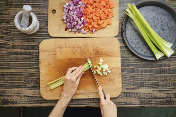 A person is chopping celery on a wooden cutting board, surrounded by diced onions and carrots. The kitchen has a warm atmosphere with natural light, emphasizing a commitment to cooking fresh food