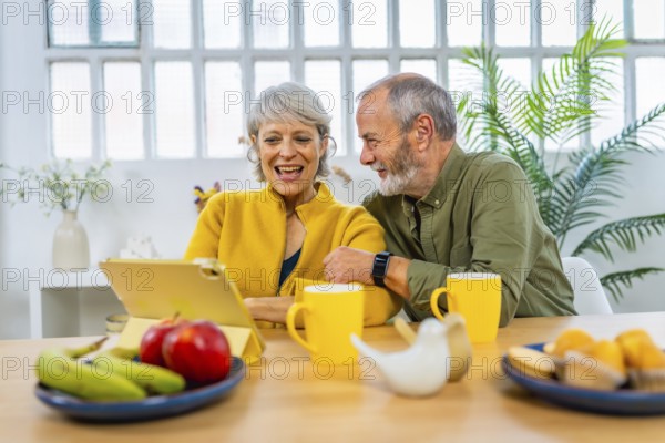 Happy senior couple using digital tablet at home while eating healthy breakfast