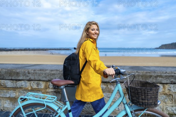 Tourist walking with her bicycle along the beach wall on a cloudy day, enjoying the fresh air and scenic views