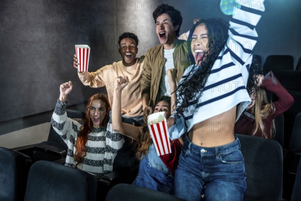 Excited friends cheering together during a movie night at the cinema, enjoying popcorn and sharing joyful moments in the darkened auditorium