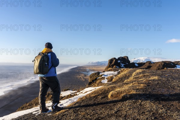 A tourist man with his back turned at the viewpoint of Dyrholaey beach in the cold winter with snow in Iceland