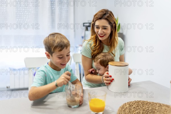 Mother holding a baby and having breakfast with her son at home in the morning
