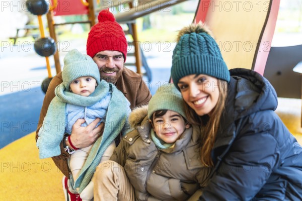 Smiling family wearing winter clothes and woolen hats, spending time together at the playground
