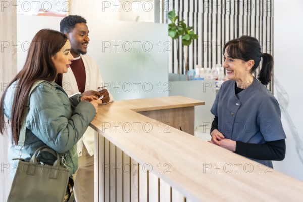 Interracial couple filling out paperwork at the reception desk of a modern dental clinic, interacting with the friendly receptionist