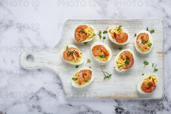 Boiled eggs stuffed with yolk and seasoned with mayonnaise, stuffed eggs with shrimp, on a white wooden chopping board, selective focus, close-up, without people