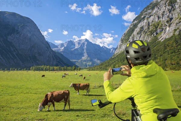 A biker uses her mobile phone to photograph the Großer Ahornboden and the grazing cows, Großer Ahornboden, Karwendel Mountains, Tyrol, Austria, Europe