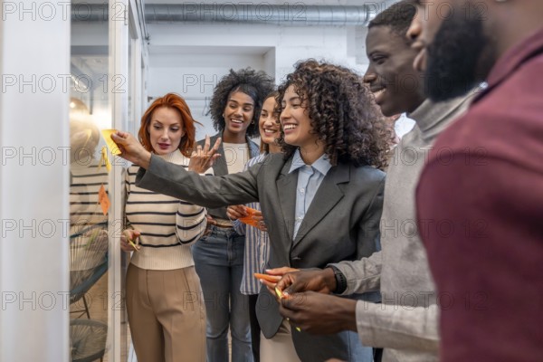 Side view of a hispanic woman using adhesive note during a creative session in startup surrounded by diverse colleagues