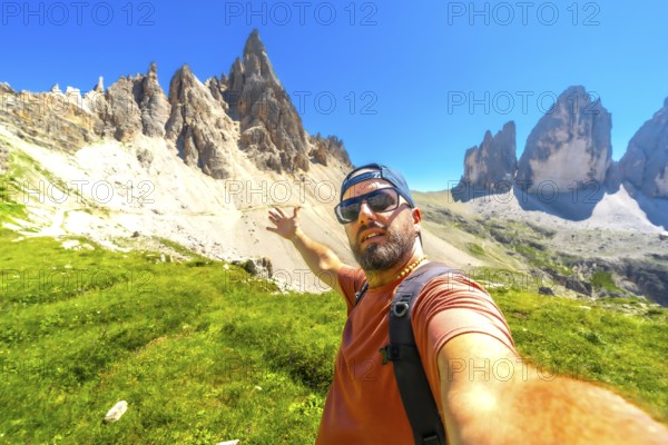 Hiker taking a selfie with the tre cime di lavaredo in the background, during a summer hike in the dolomites