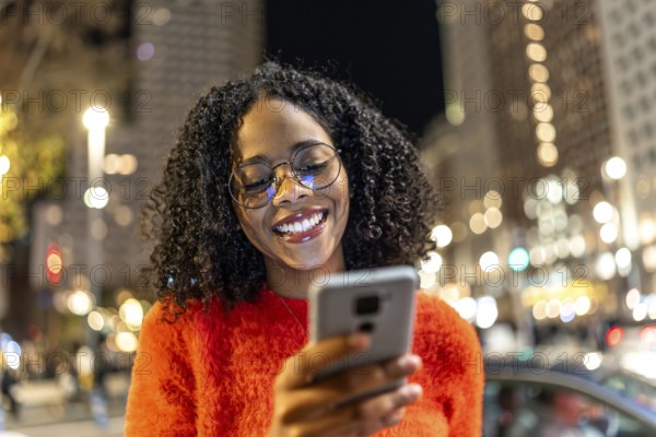 Smiling woman using her smartphone while enjoying the vibrant urban nightlife, surrounded by glowing city lights and a lively atmosphere