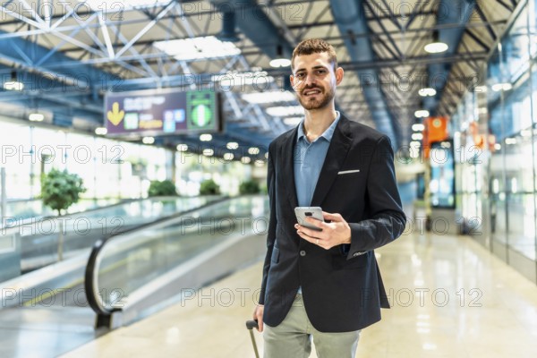 Businessman holding smartphone and pulling trolley suitcase walking through airport terminal