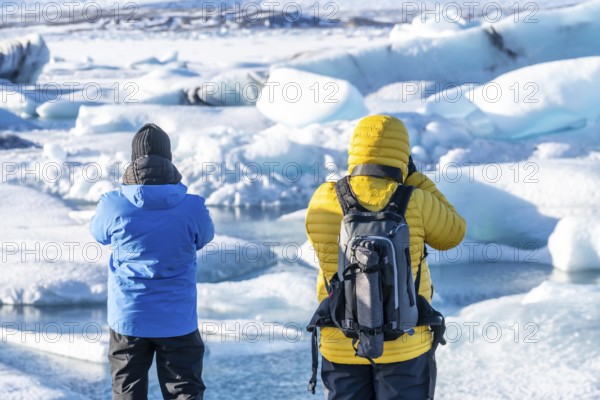 A couple of tourists looking at floating icebergs in Jokulsarlon glacier lagoon in Iceland