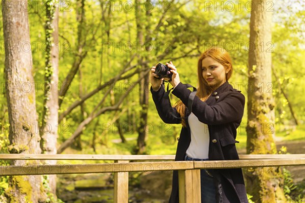 Woman photographer with a black jacket enjoying in an autumn park, taking pictures at sunset on a wooden bridge