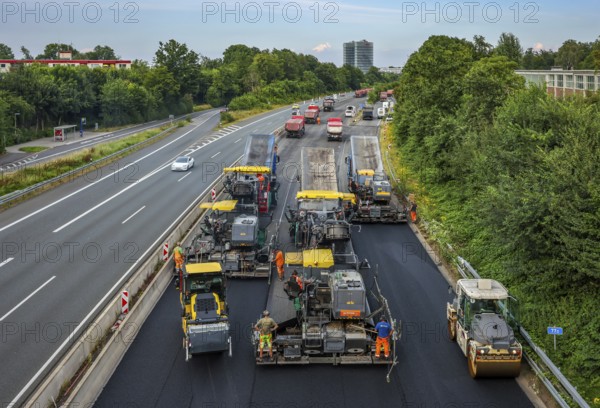 Essen, North Rhine-Westphalia, Germany, road construction, asphalt pavers and road rollers laying new, open-pored, whisper asphalt on the A52 motorway, here between the Essen-Kettwig and Essen-Rüttenscheid junctions in the direction of Dortmund. Skyline of Essen with the EON headquarters building in the background, Europe