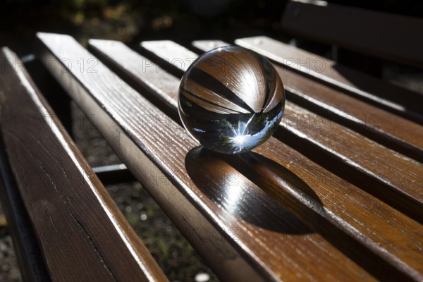 Glass ball lying on a bench with wooden slats, reflecting the sun, Saxony, Germany, Europe