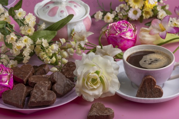 Coffee mug with heart-shaped chocolate and flowers on a pink background, Valentine's Day