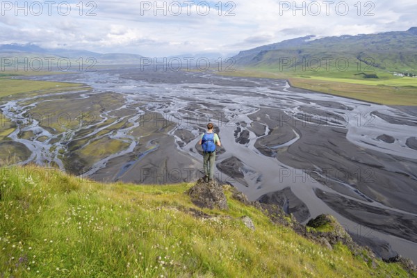 Hiker, young man on a hill, view over alluvial land, meandering river, Dímonarhellir, Suðurland, Iceland, Europe