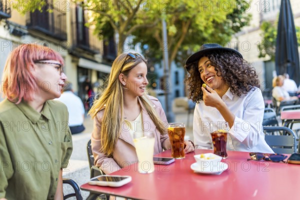 Modern diverse women sitting on sidewalk bar drinking and eating snacks in the city