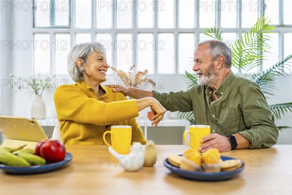 Frontal view of a caucasian happy senior couple laughing while enjoying breakfast at home