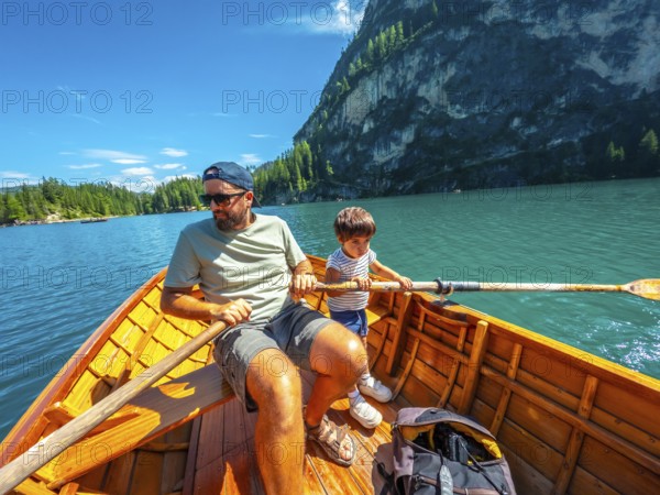Father and son enjoying a summer day rowing a wooden boat on lake braies with the stunning dolomites in the background
