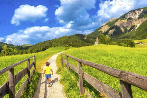 Young tourist walking on a path towards the famous st. Magdalena church in val di funes in the italian dolomites on a sunny summer day