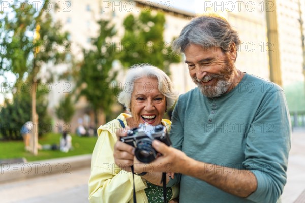 Happy senior couple looking at the photos in a camera standing in the city street