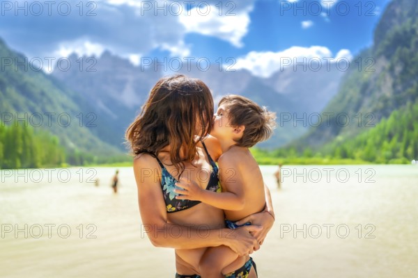 Mother embracing and kissing her son while enjoying summer vacation at lago di landro, surrounded by the breathtaking dolomites