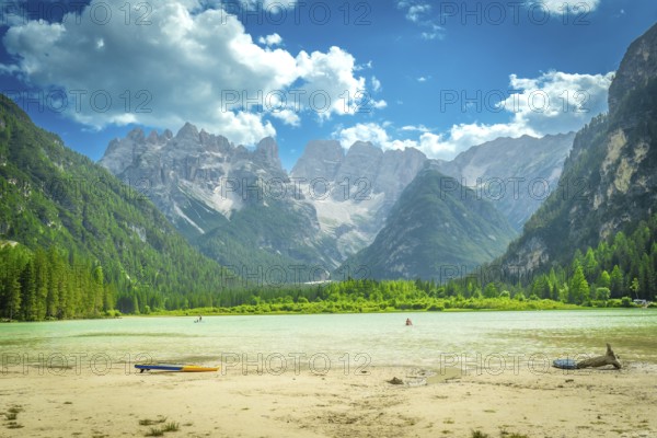 Tourists swimming and paddleboarding in the turquoise waters of lago di landro, surrounded by the breathtaking peaks of the dolomites on a sunny summer day
