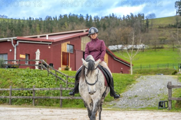 Frontal view of a young woman riding a white horse in a calm equestrian center