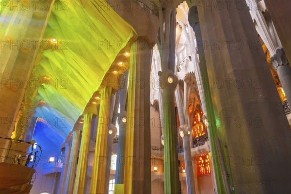 Sunlight illuminates colorful stained glass windows, casting vibrant hues onto architectural columns inside sagrada familia in barcelona