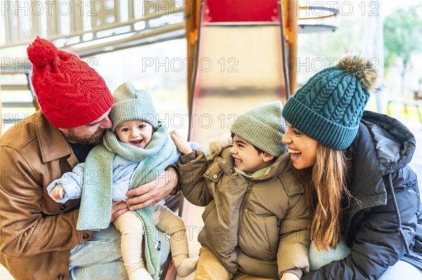 Cheerful family bundled in warm winter clothes, enjoying playful moments together on a playground slide, sharing laughter and joy