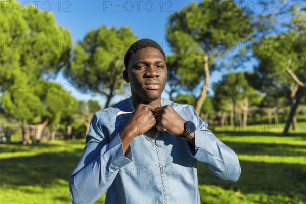 Young african man wearing traditional dashiki attire, adjusting his collar in a serene park setting
