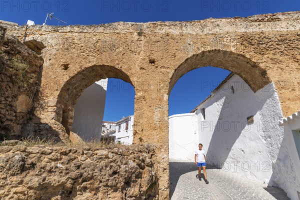 A man walks through an arch under a historic aqueduct in the white village of Yunquera, Sierra de las Nieves National Park, Malaga, Andalusia, Spain, Europe