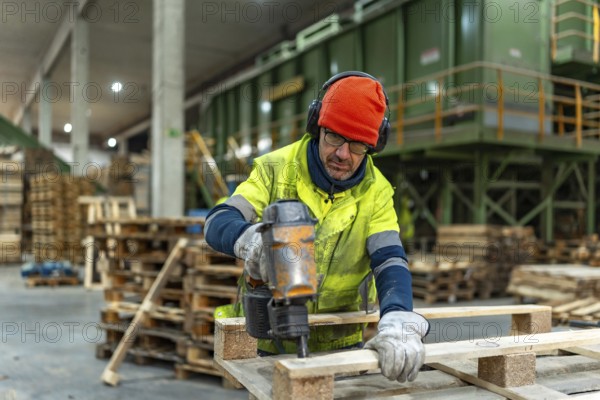 Man worker using compressed air gun to repair pallets in a recycling plant