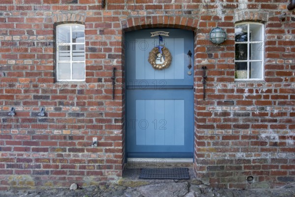 Blue wooden door in red brick wall with two windows and decorations, Föhr, Nordfriesland, Schleswig-Holstein, Germany, Europe