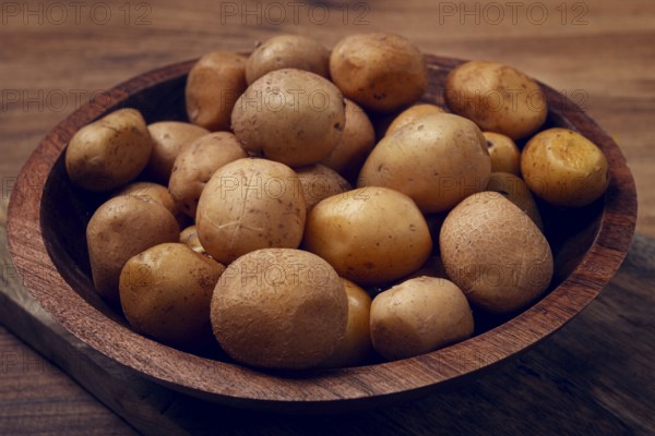 A wooden bowl filled with freshly harvested small potatoes sits on a rustic wooden surface, showcasing their natural earthy tones and textures, perfect for various culinary dishes