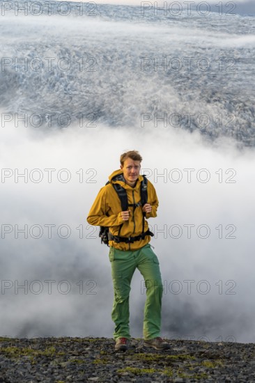 Young man in front of impressive landscape at sunset, fog, clouds moving around, glacier ice of the glacier tongue Kötlujökull, glacier Myrdalsjökull, Pakgil, Iceland, Europe