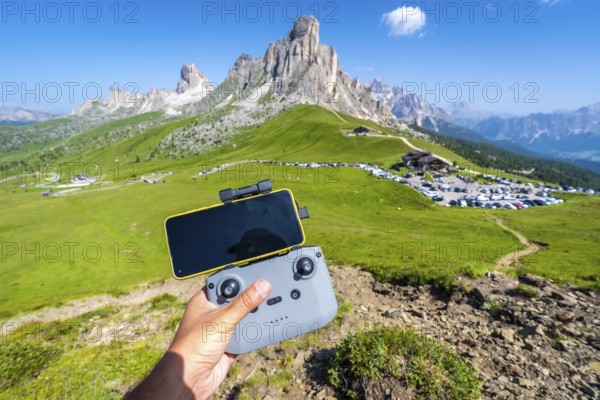Hand piloting a drone with a smartphone attached to the controller in the scenic landscape of giau pass, dolomites, italy, during a sunny summer day