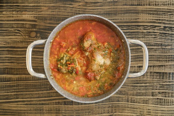 A hearty turkey stew with vibrant vegetables is simmering in a pot on a wooden surface. The rich red broth and tender meat suggest a comforting meal perfect for a gathering on a cozy day.