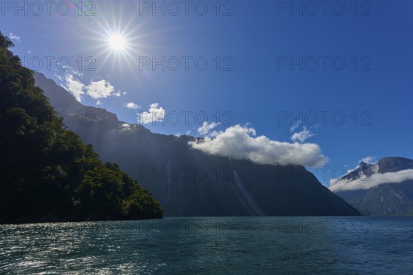 Sunbeams shine over majestic mountains and a calm lake under a clear sky, summer, Milford Sound, Te Anau, Fiordland National Park, South Island, New Zealand, Oceania