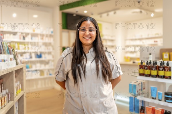 Portrait of a cheerful young female pharmacist with eyeglasses and uniform standing smiling at camera in the store